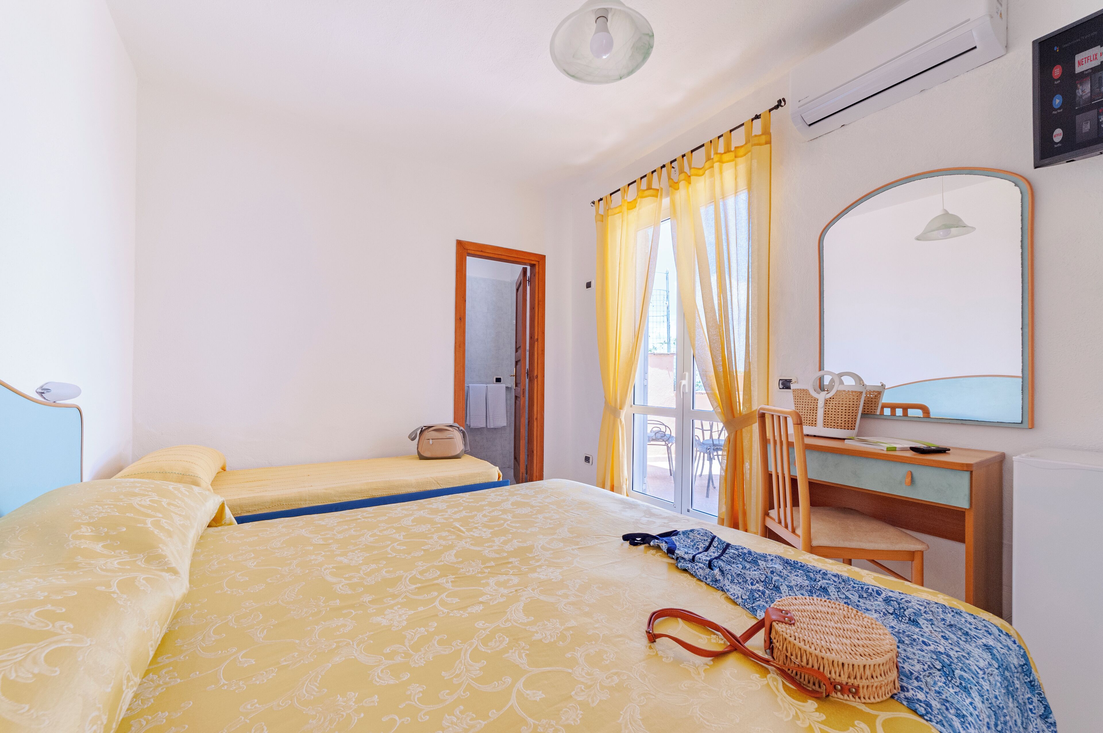 A bedroom with two beds, a desk, a chair, a mirror, and a window with curtains.