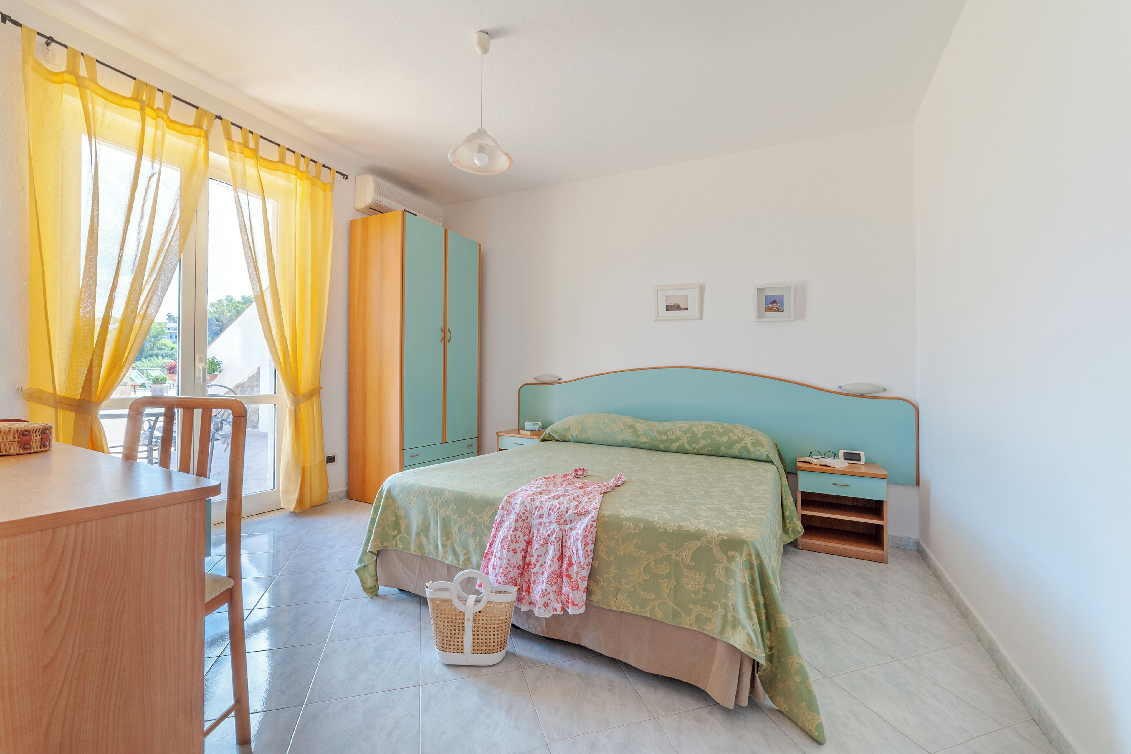 A bedroom with a bed, a desk, a chair, a nightstand, and a window with curtains.