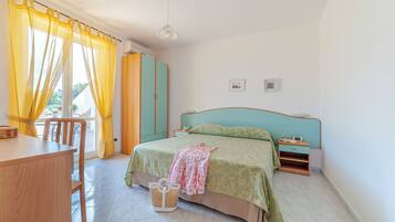 A bedroom with a bed, a desk, a chair, a nightstand, and a window with curtains.