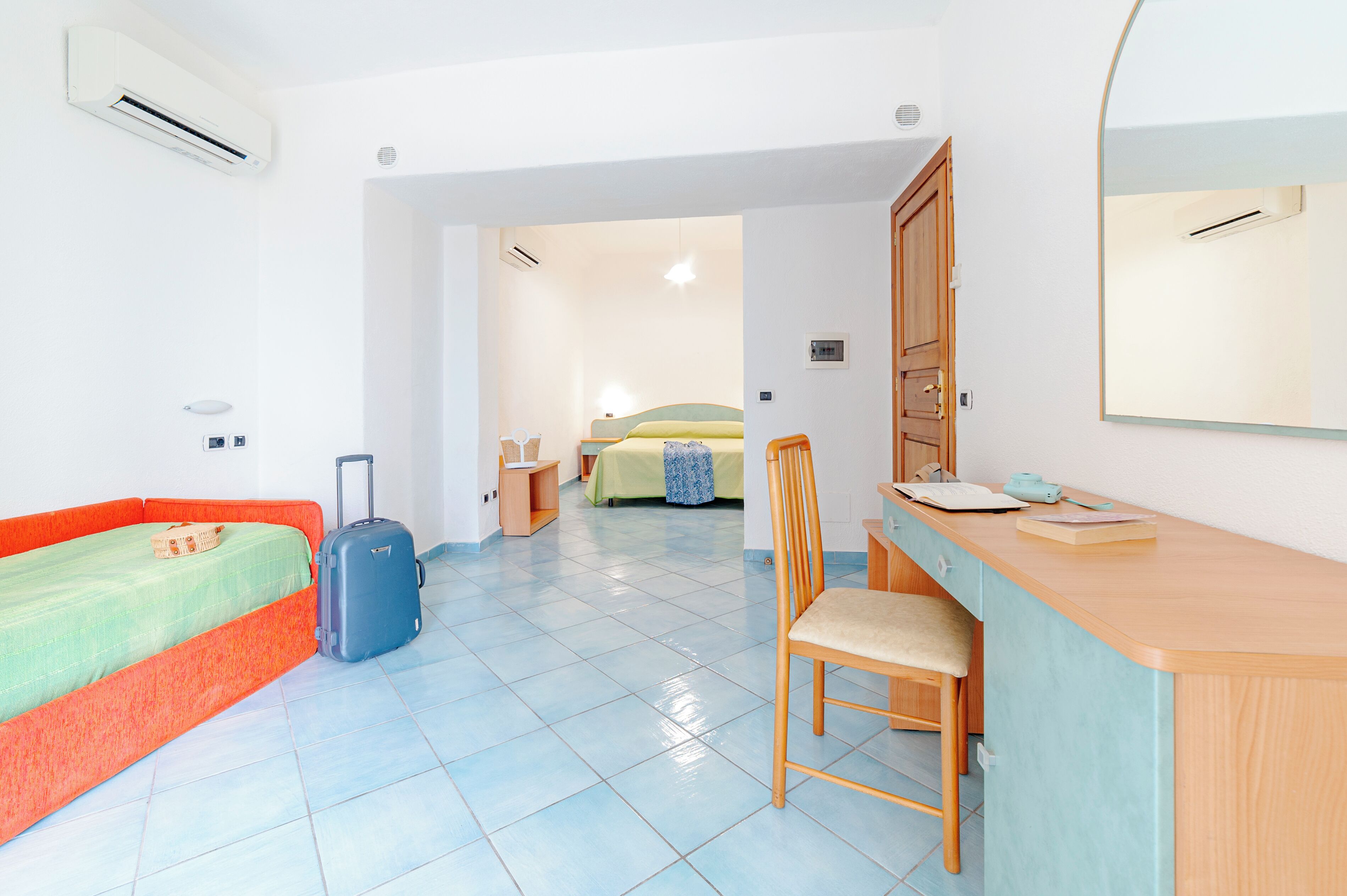 A room with a bed, a desk, a chair, and a suitcase.