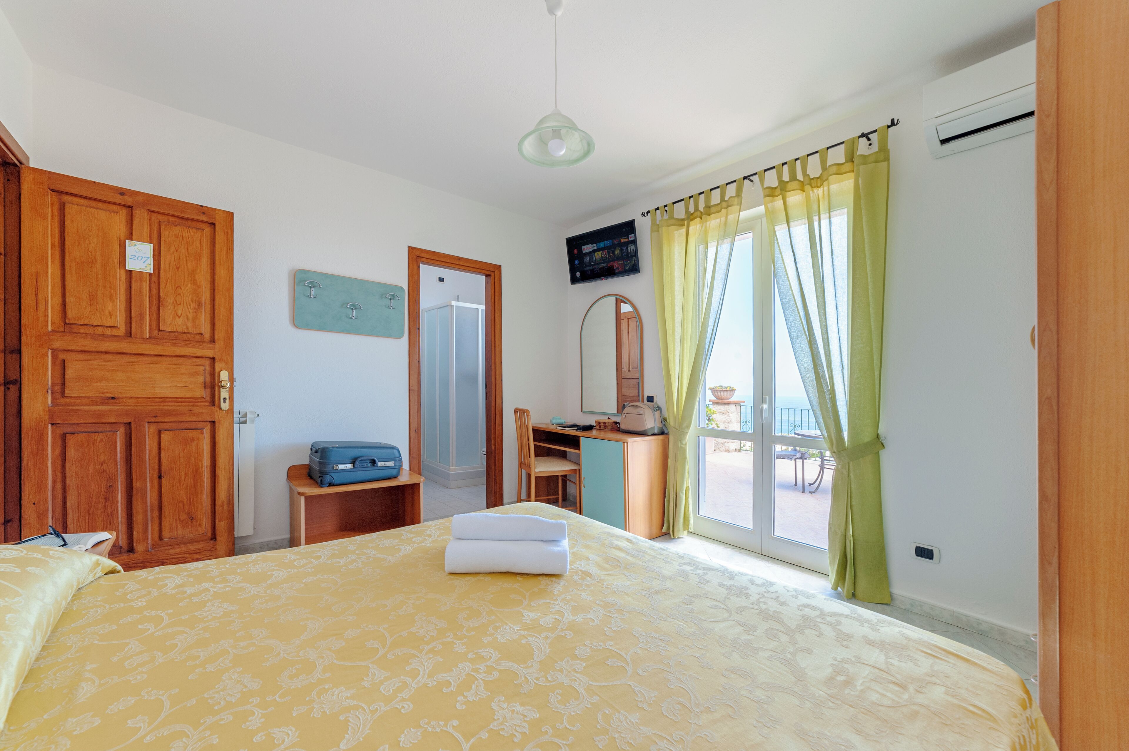 Una camera d'albergo con un letto, una scrivania, una sedia, una televisione e una finestra con tende.