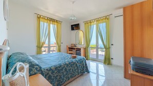 Une chambre d’hôtel avec un lit, un bureau, une chaise et une valise posée sur une étagère.