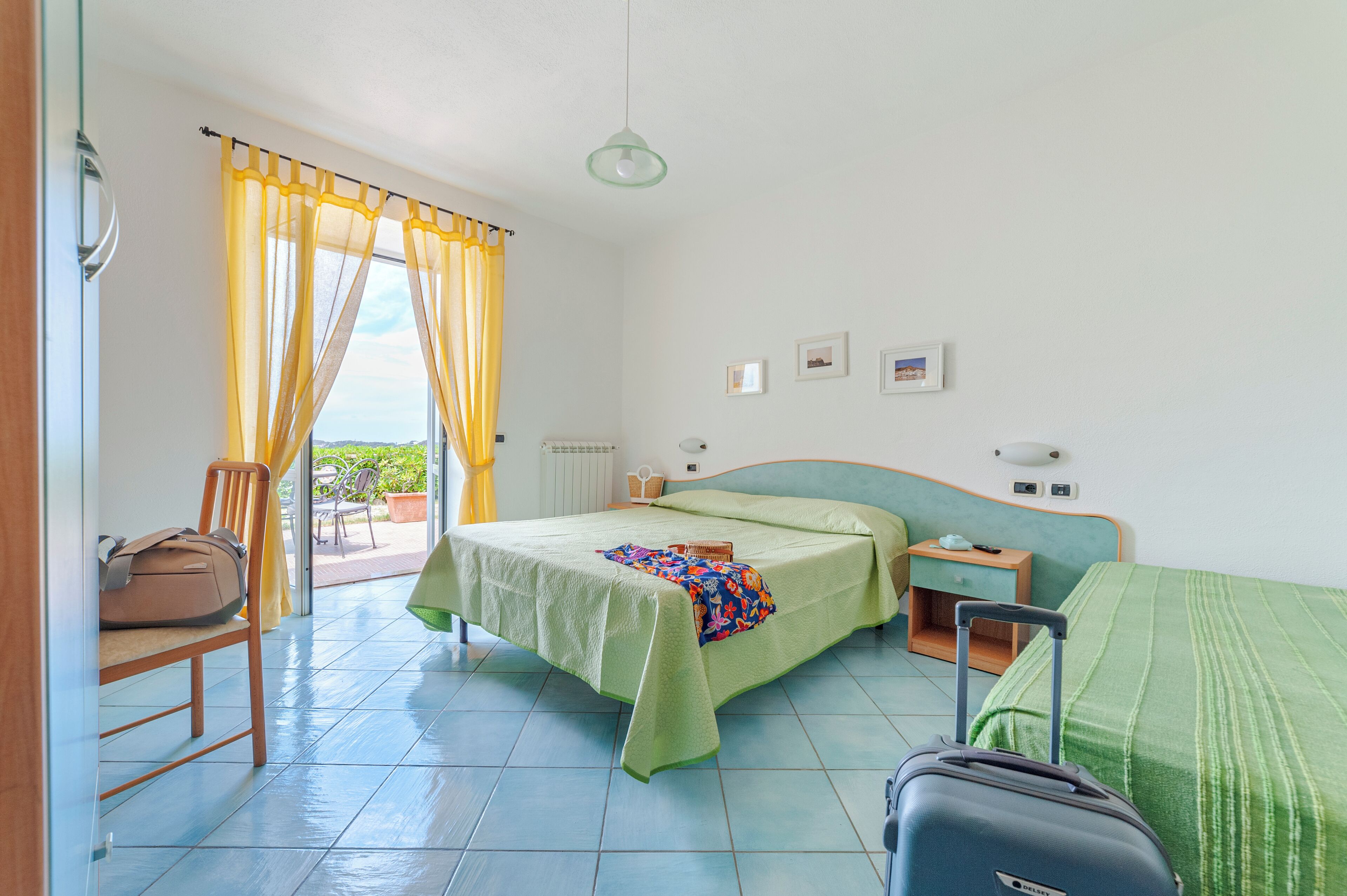A hotel room with a bed, a suitcase, a chair, a nightstand, and a view of the outdoors.