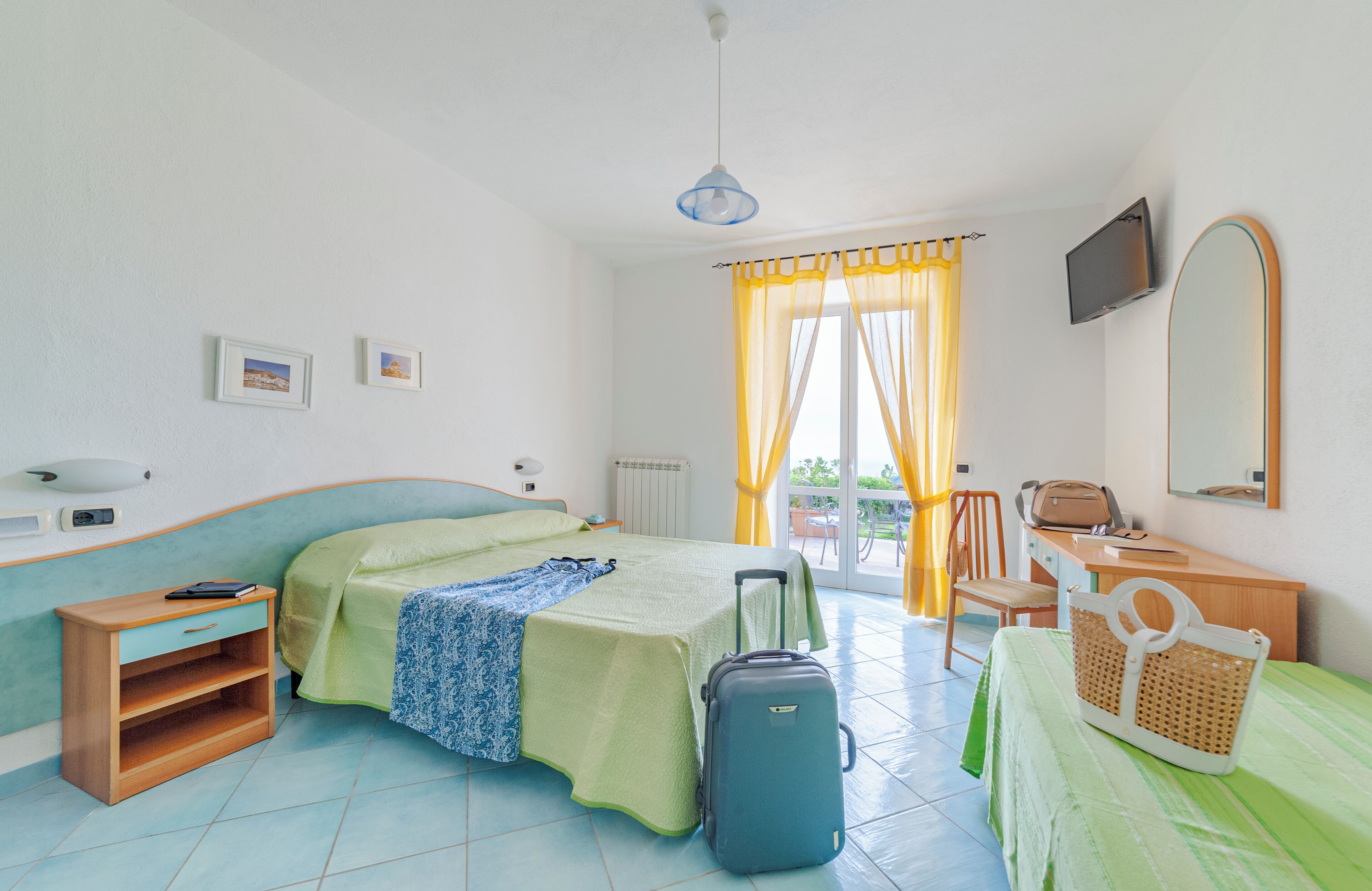 A hotel room with a bed, a desk, a chair, a suitcase, and a television.