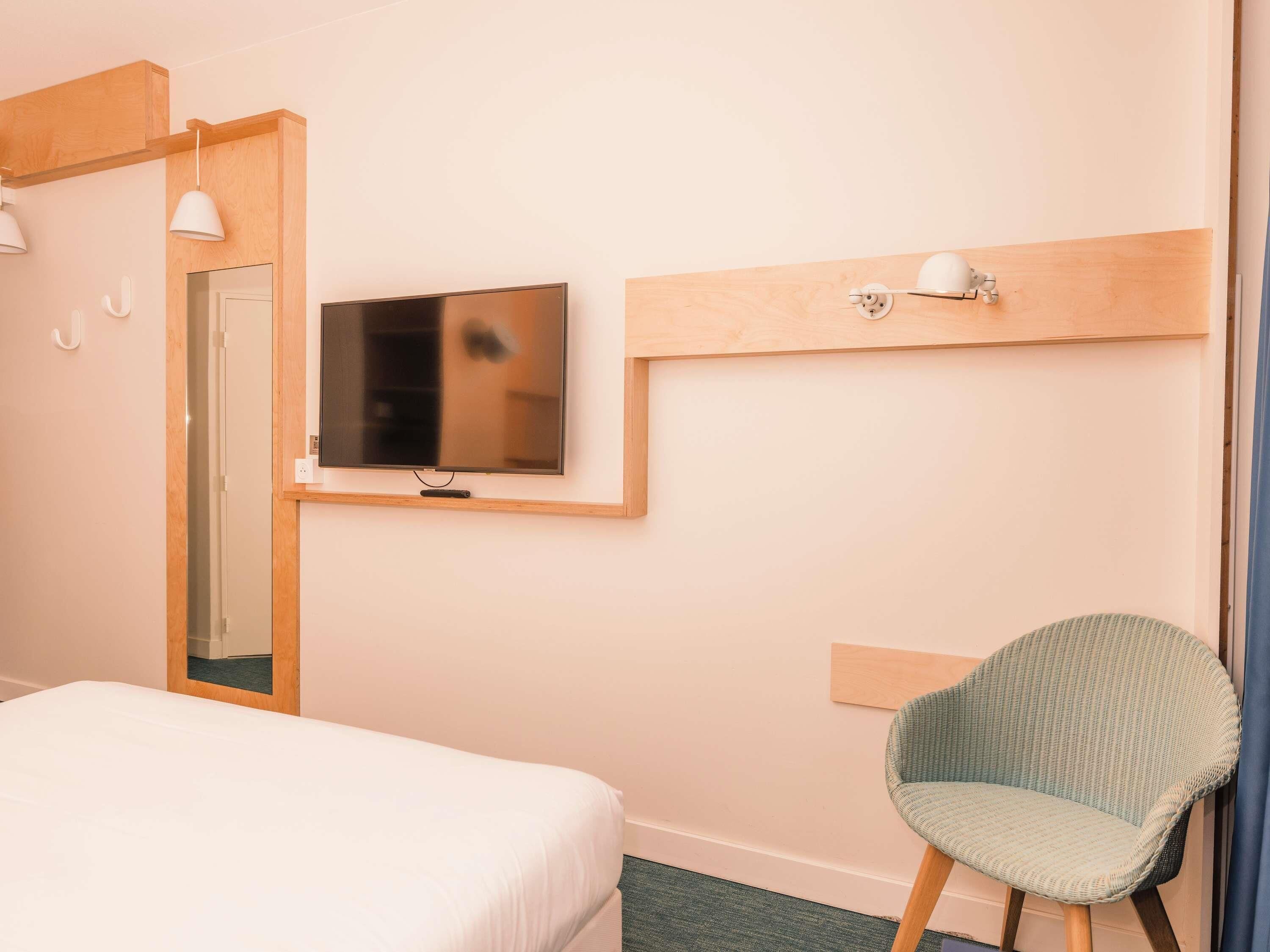 Een hotelkamer met een bed, een televisie aan de muur, een stoel en een houten hoofdeinde.