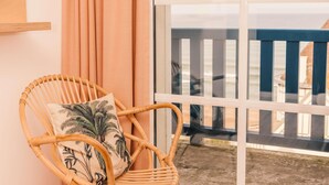 A wicker chair with a palm leaf pillow, positioned by a window with a view of a deck and railing. - Hotel ibis Styles Deauville Villers Plage (Villers-sur-Mer)