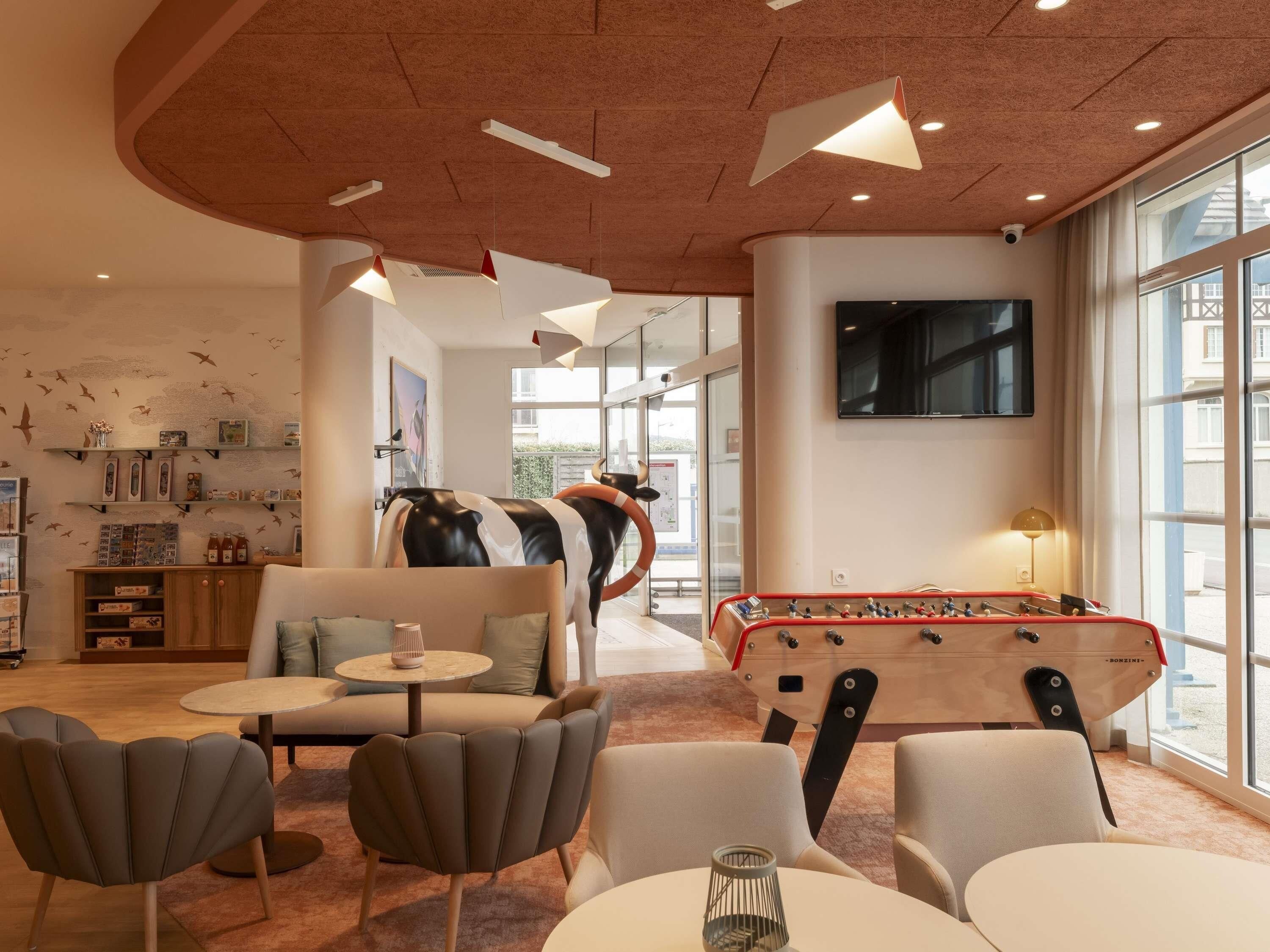 Un salon moderne doté d’un baby-foot, de sièges confortables et d’une grande fenêtre laissant entrer la lumière naturelle.