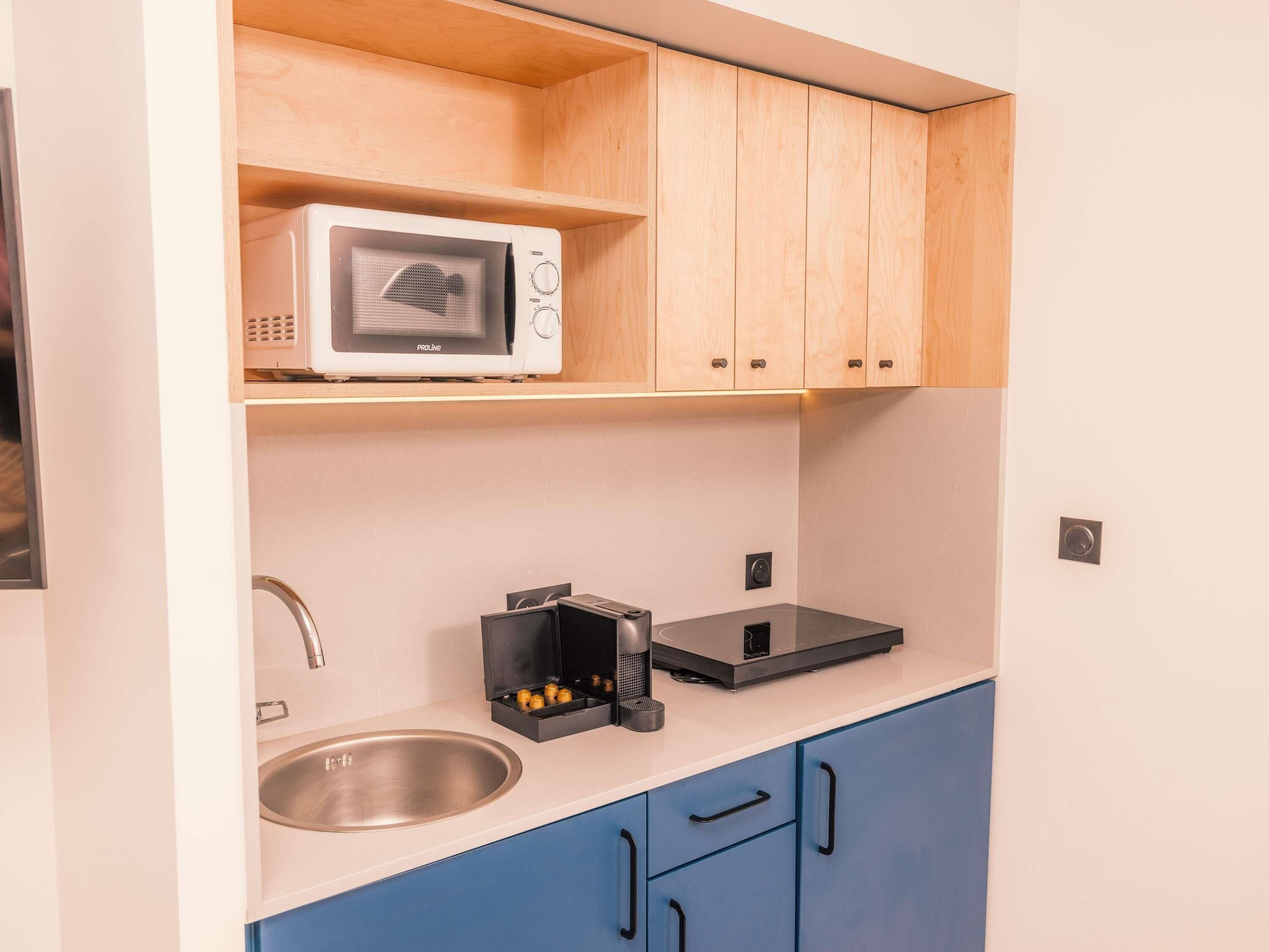 Une cuisine de taille réduite, équipée d’un four à micro-ondes, d’un évier et de meubles de rangement bleus.