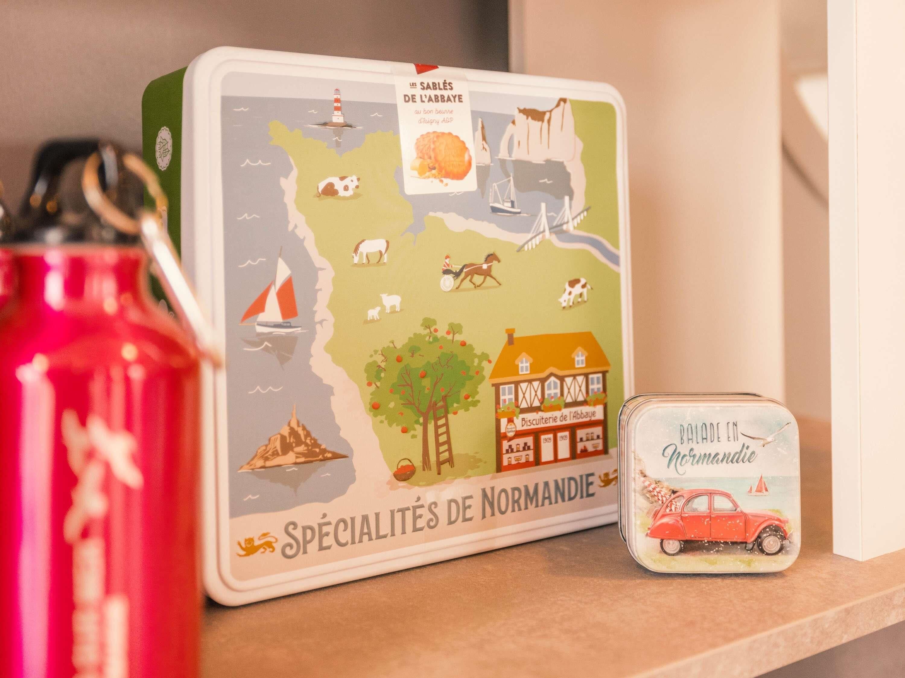A map of Normandy specialties, a red container, and a small tin with a car illustration.
