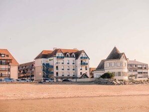 A coastal building with multiple balconies, a prominent tower, and a sandy foreground.
