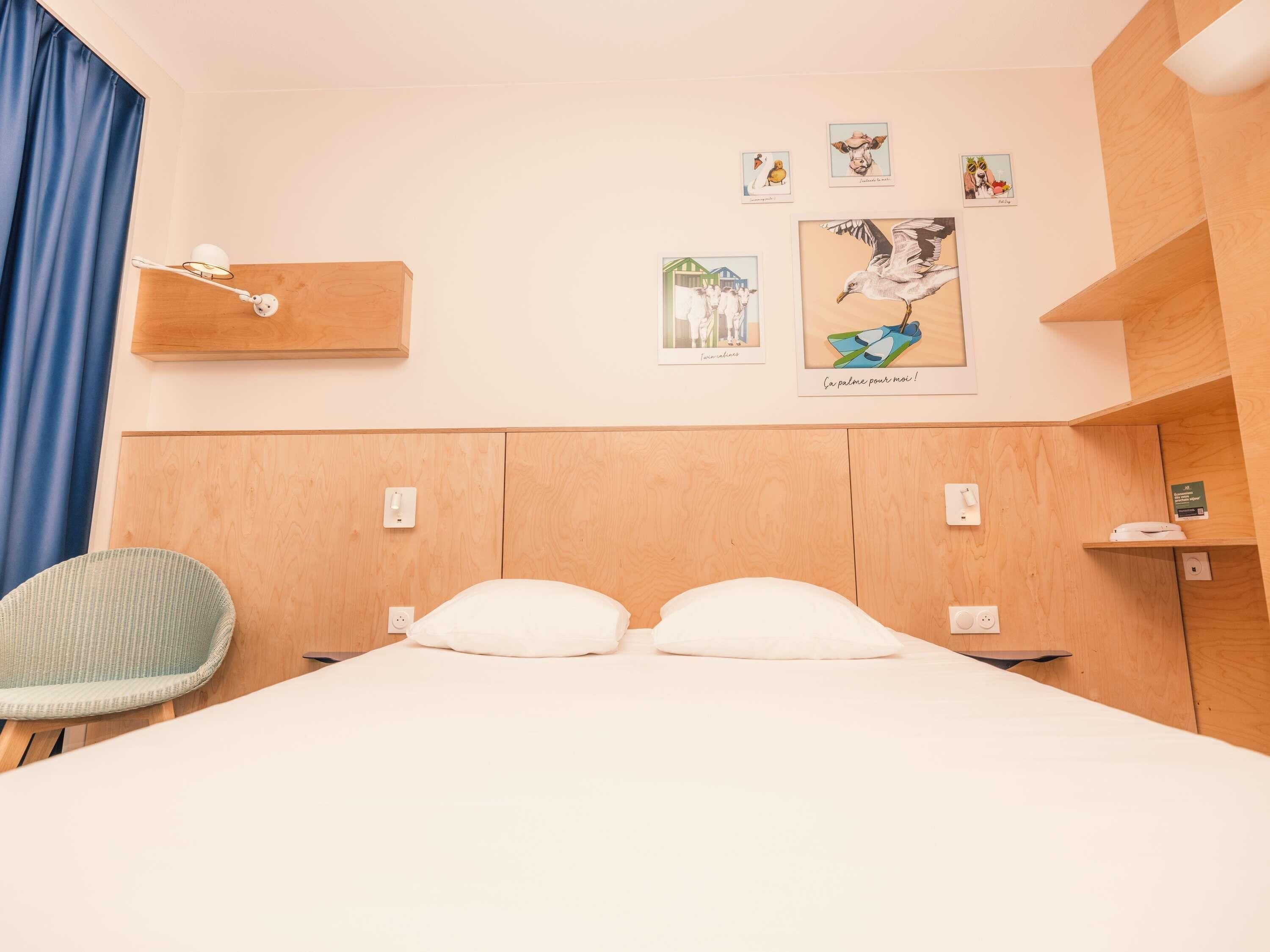 A hotel room with a bed, a chair, and wall art.