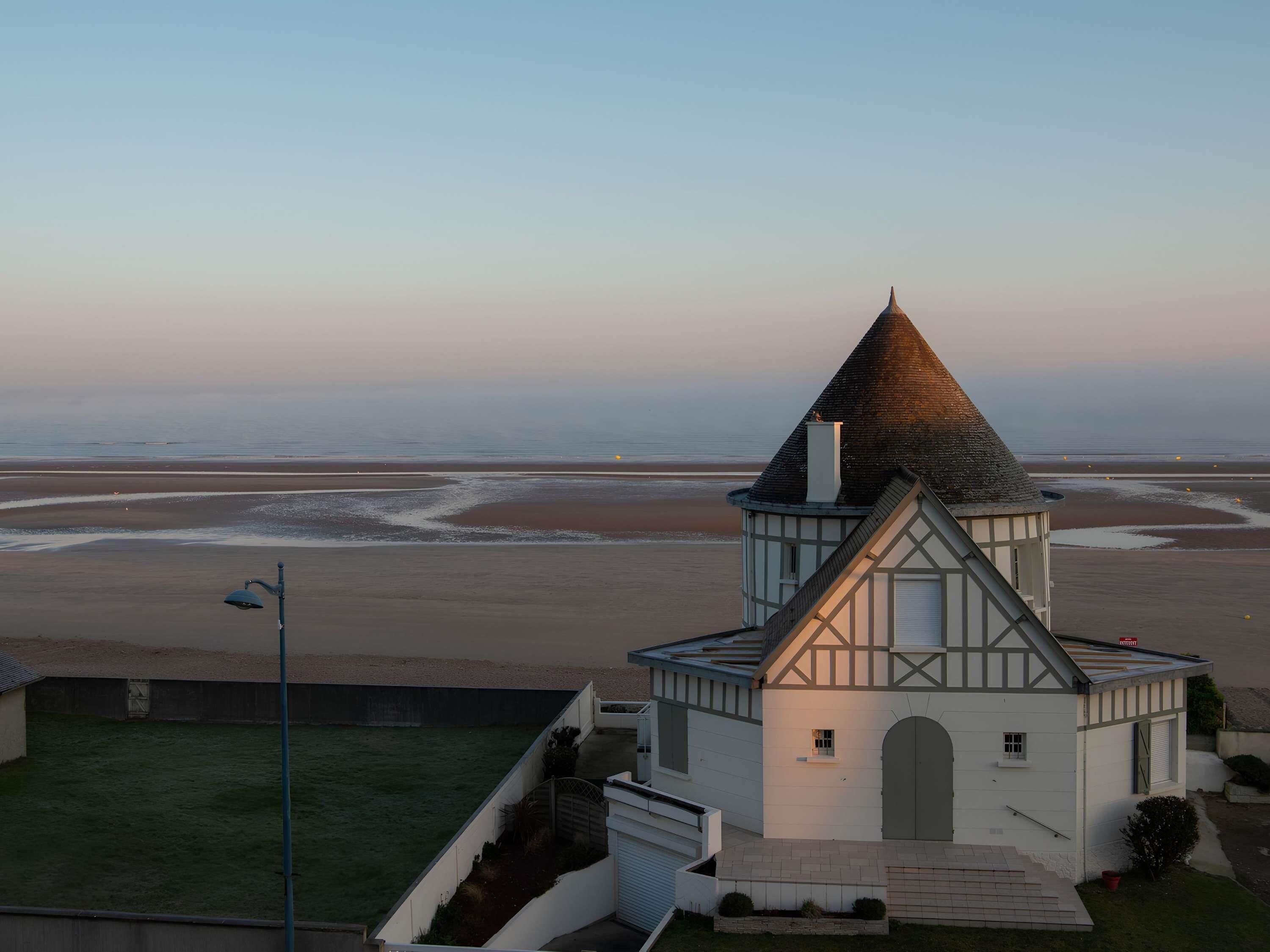 Um pequeno edifício branco com telhado cônico próximo à praia.
