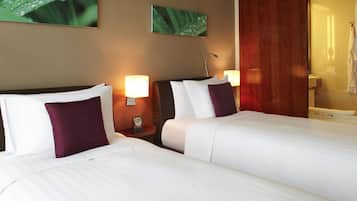 Habitación de hotel con dos camas, una mesita de noche con lámpara, una puerta de madera y un espejo.