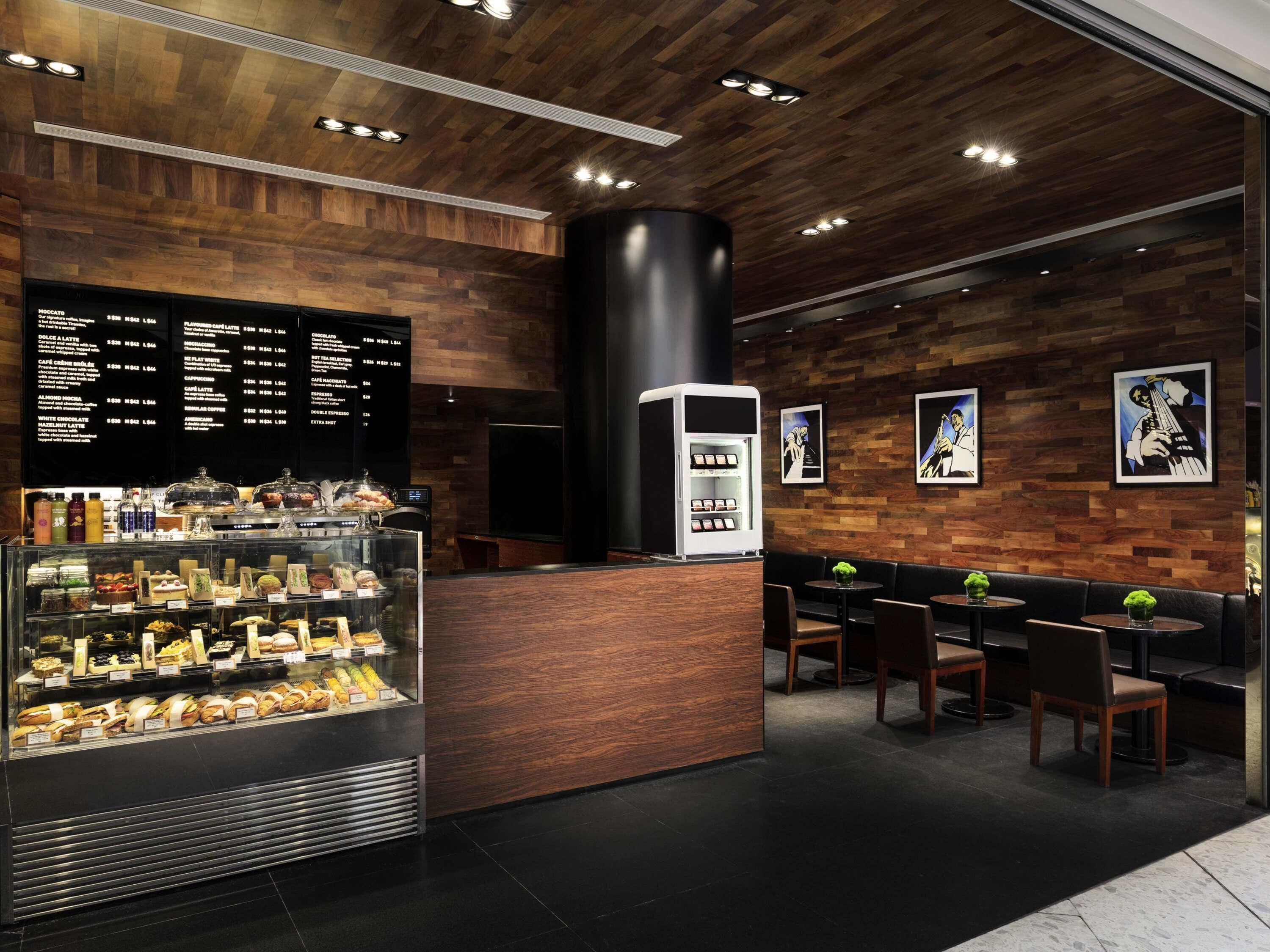 A modern cafe with a wooden interior, a menu board, a display case with pastries, and seating area.