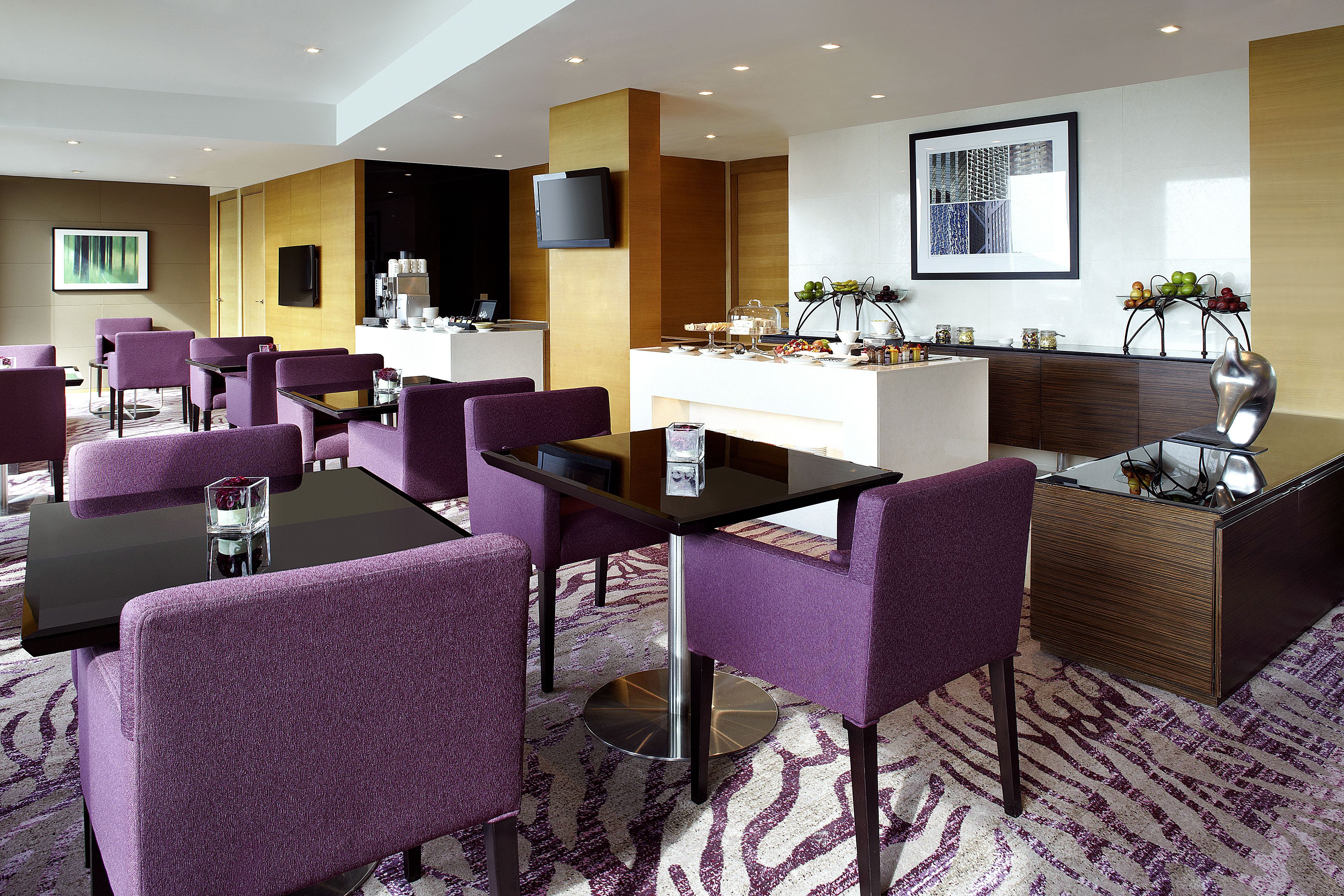 A modern hotel lobby with purple seating, a reception desk, and a large TV screen.