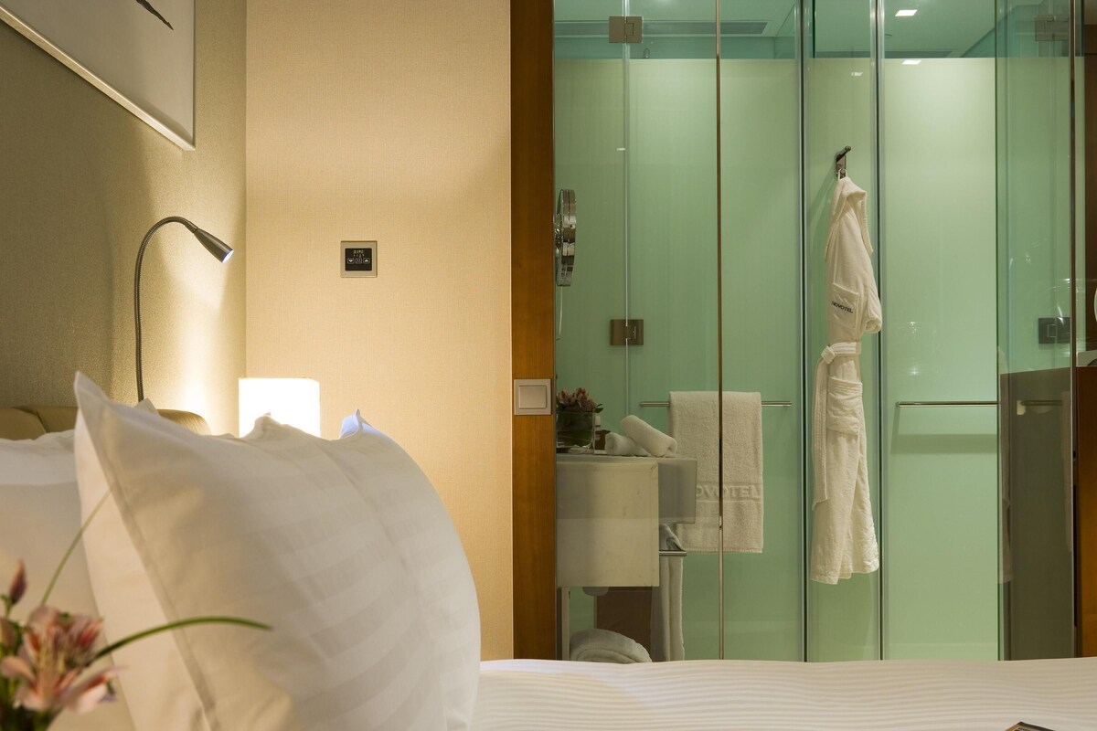 Une chambre d’hôtel avec un lit, une lampe de chevet, une douche en verre et un peignoir accroché à la porte de la douche.