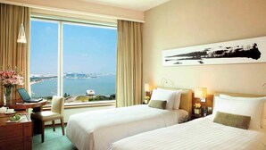 Habitación de hotel con dos camas, un escritorio con una computadora portátil, una silla y vistas a un cuerpo de agua y al paisaje urbano.