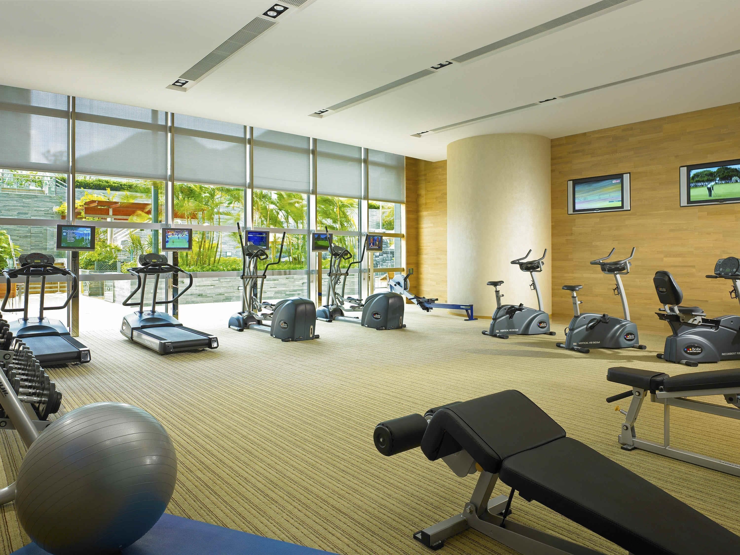 Ein Fitnessraum mit Laufbändern, Crosstrainern, einem Rudergerät und einer Langhantelbank.