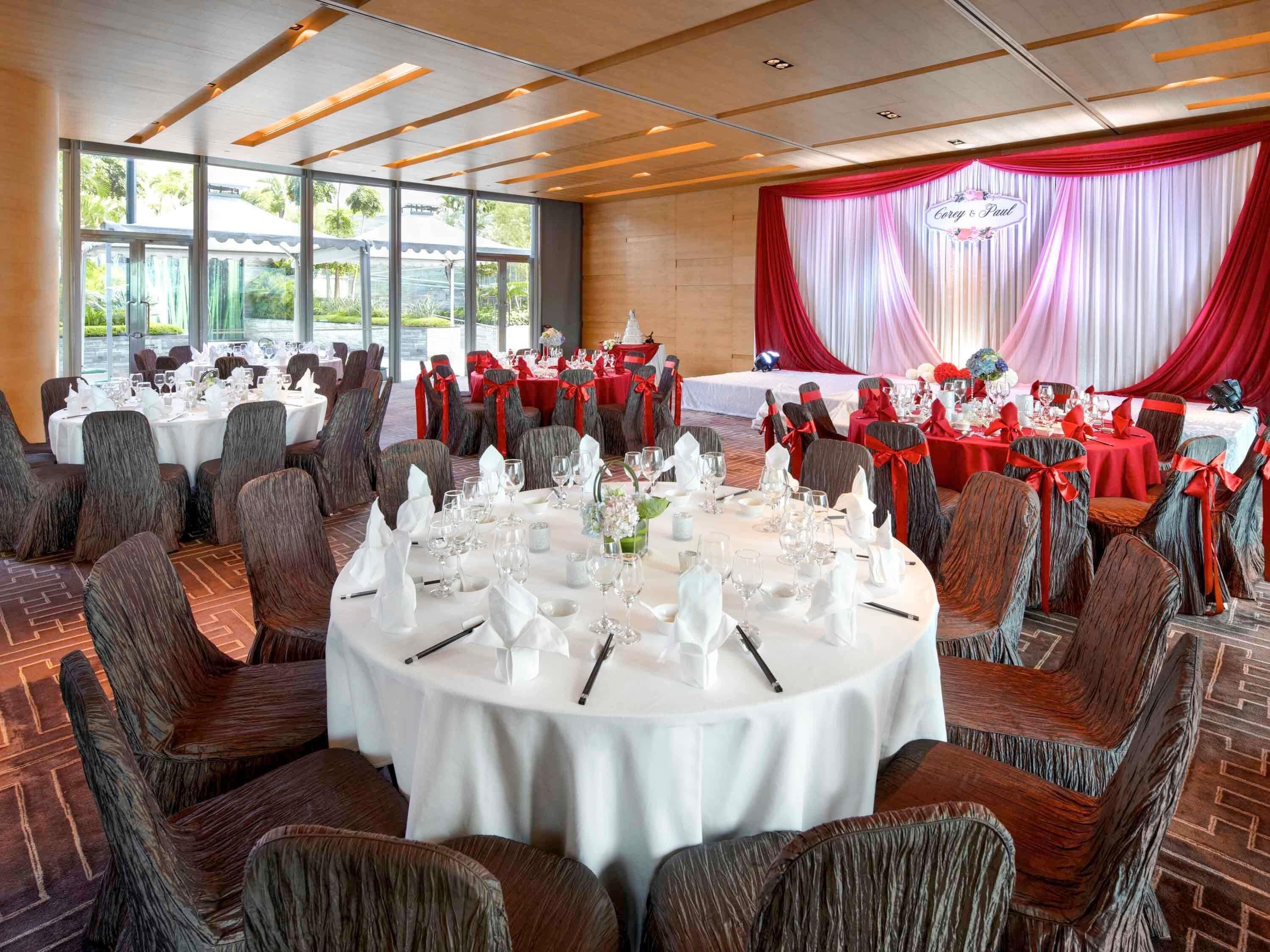 A banquet hall with round tables, red and white drapes, and a stage.