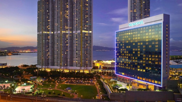 Un hotel Novotel con fachada de vidrio moderna, rodeado de edificios altos y vistas al agua.