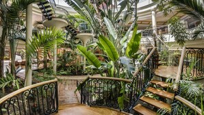 A multi-level atrium with a central staircase surrounded by lush tropical plants and a glass ceiling.