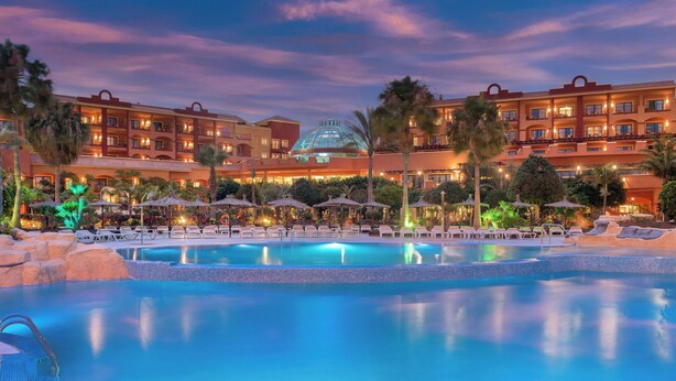 A hotel with a swimming pool, palm trees, and a large building with a dome.