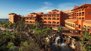 A resort with multiple-story buildings, a central courtyard with palm trees, and a waterfall feature.