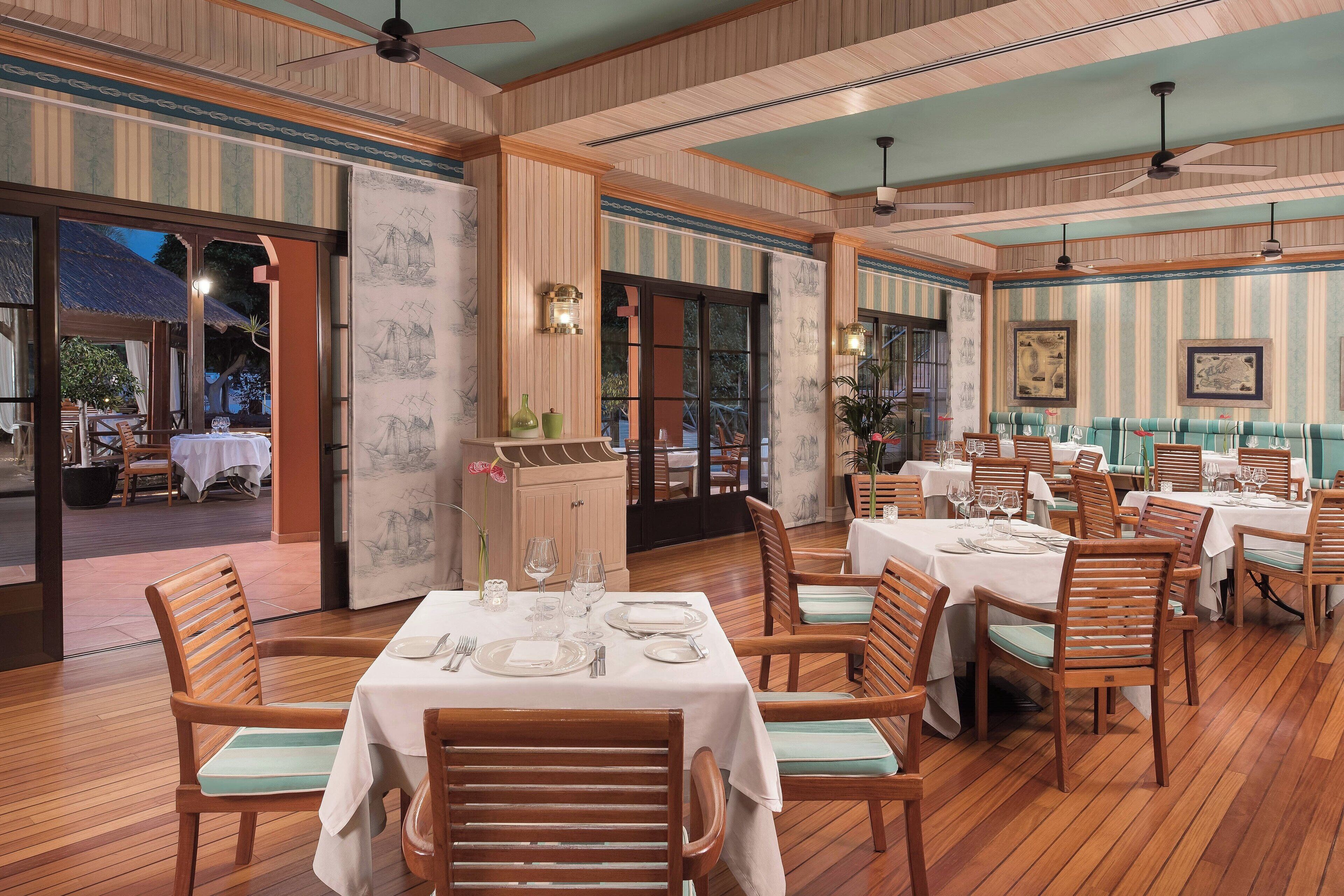 A restaurant with wooden flooring, striped walls, and tables set for dining.