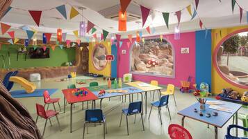 Una aula de jocs infantil amb parets de colors, taules, cadires i diferent material de joc.