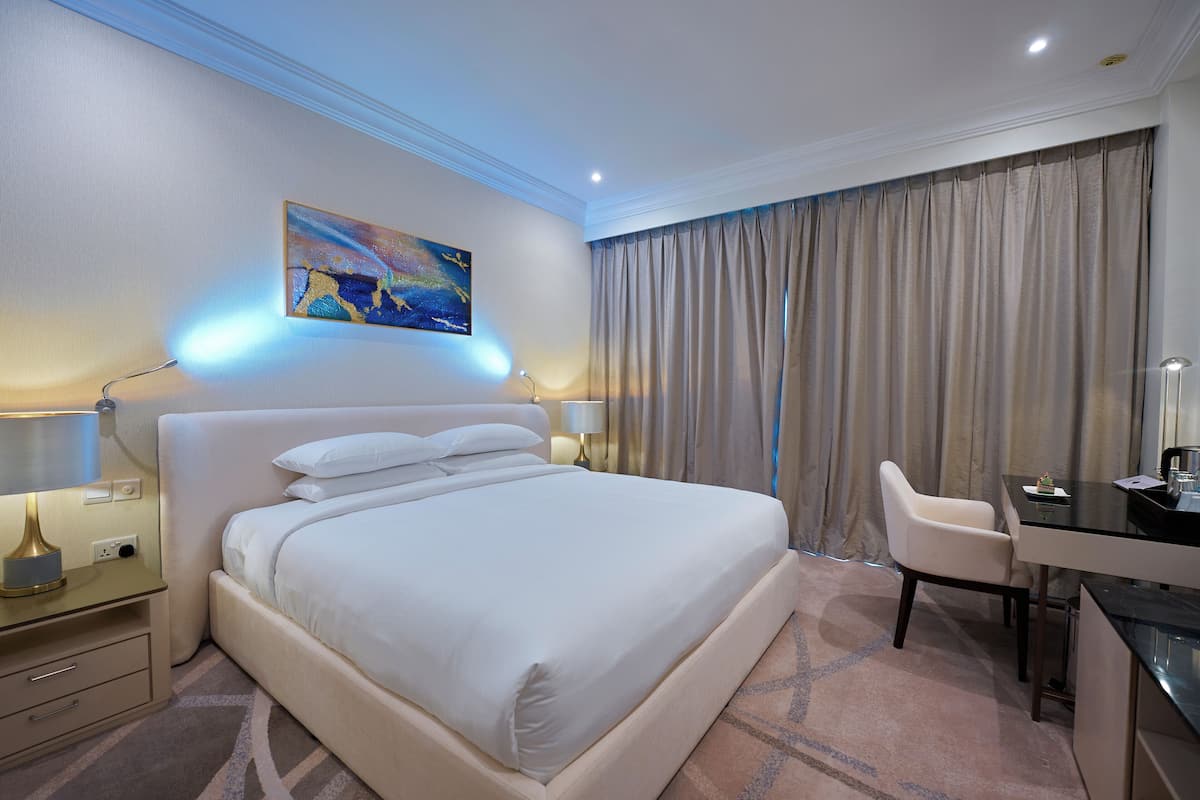 Habitación de hotel con una cama grande, un escritorio y una silla. Hay un cuadro en la pared y una lámpara en la mesita de noche.
