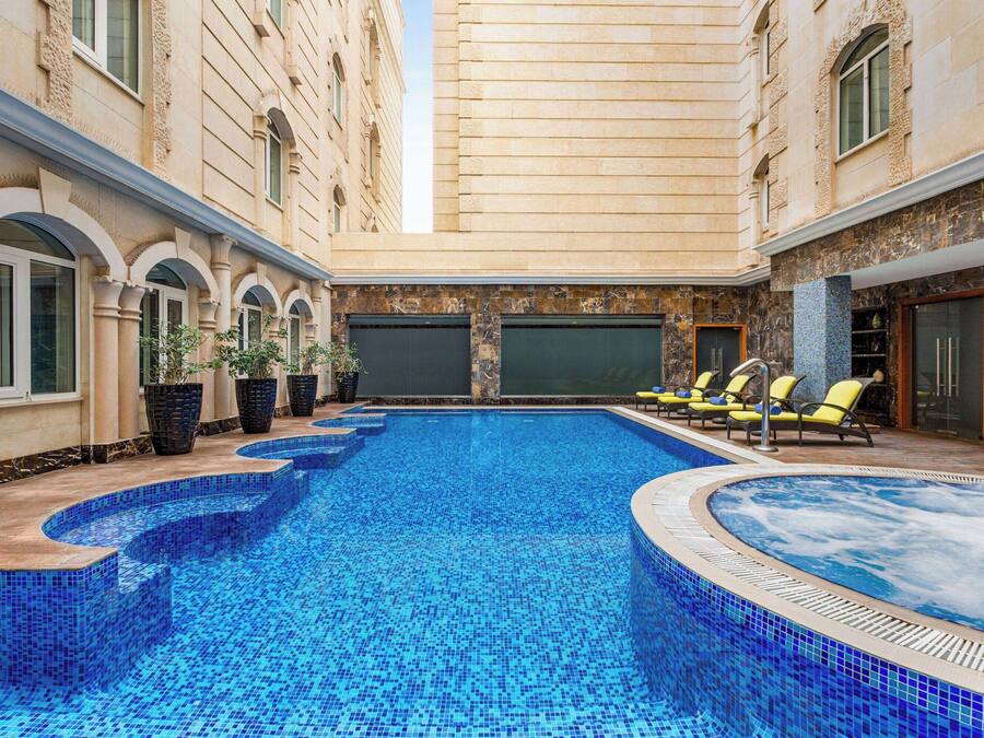 Una piscina con bordes azules de azulejos, rodeada de sillas de descanso y plantas en macetas.