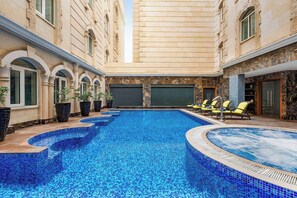 A swimming pool with tiled blue edges, surrounded by lounge chairs and potted plants. - Grand Regency Doha, Trademark Collection by Wyndham (Doha)