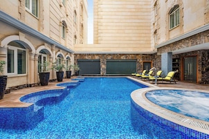Una piscina con bordes azules de azulejos, rodeada de sillas de descanso y plantas en macetas.