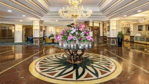 Un amplio vestíbulo con una mesa redonda central decorada con flores, un candelabro y un suelo de mármol pulido.