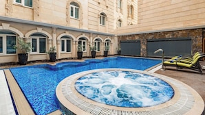 A swimming pool with a hot tub, lounge chairs, and potted plants.