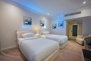A hotel room with two beds, a desk, a chair, and artwork on the walls. - Grand Regency Doha, Trademark Collection by Wyndham (Doha)