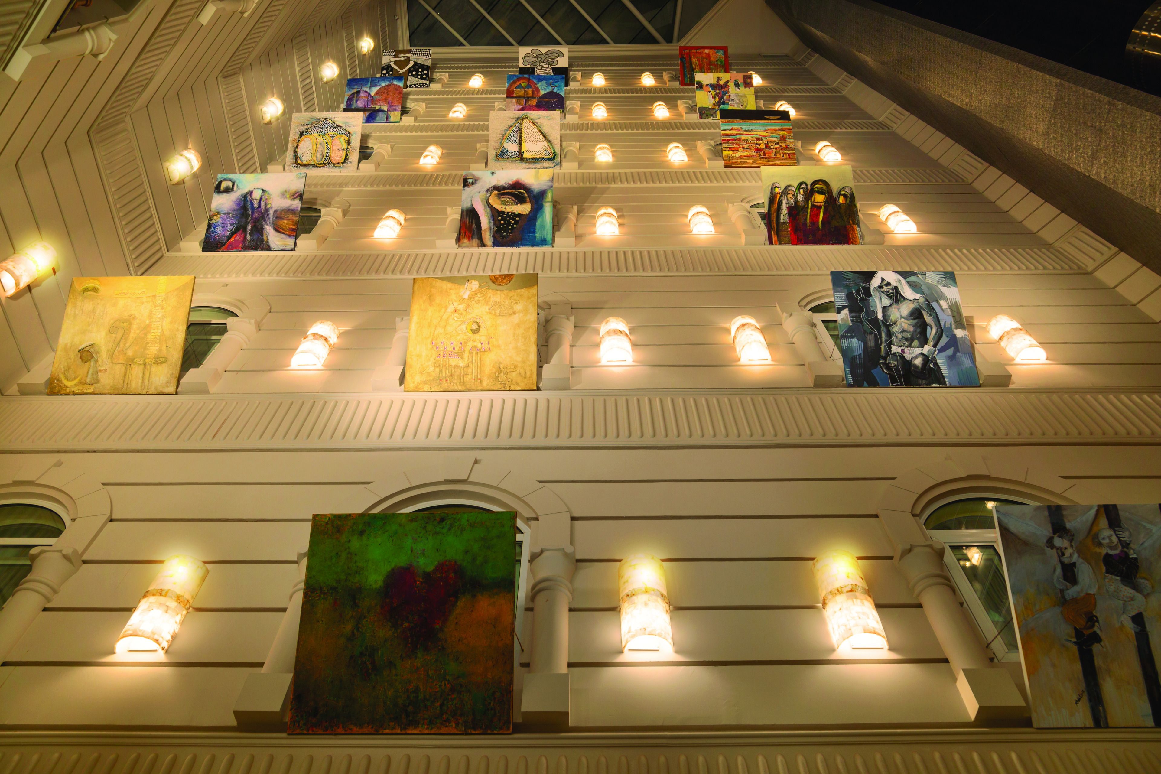 A building with multiple levels, each adorned with various artworks and illuminated by wall-mounted lights.