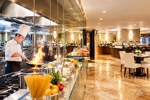 A chef cooking with flames in a modern kitchen with a buffet area in the background. - Grand Regency Doha, Trademark Collection by Wyndham (Doha)