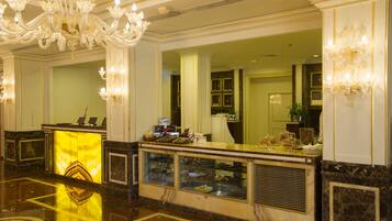 Un vestíbulo de hotel con mostrador de recepción, una araña de cristal y una vitrina.