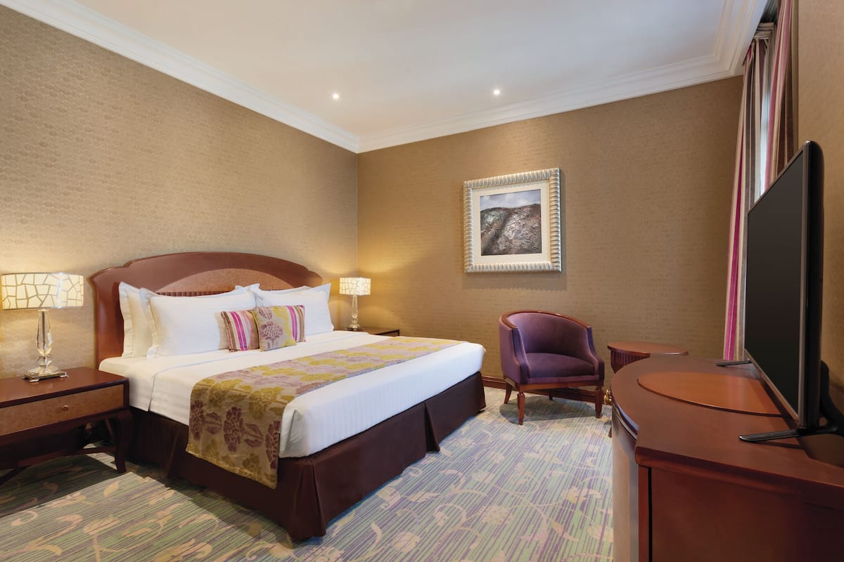 Una habitación de hotel con una cama grande, un escritorio con televisión de pantalla plana, una silla y un cuadro en la pared.