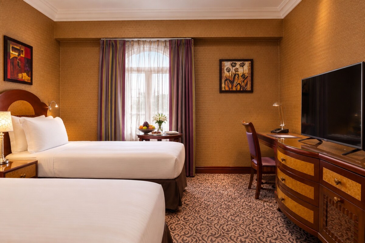 A hotel room with two beds, a desk with a chair, a television, and a window with curtains.