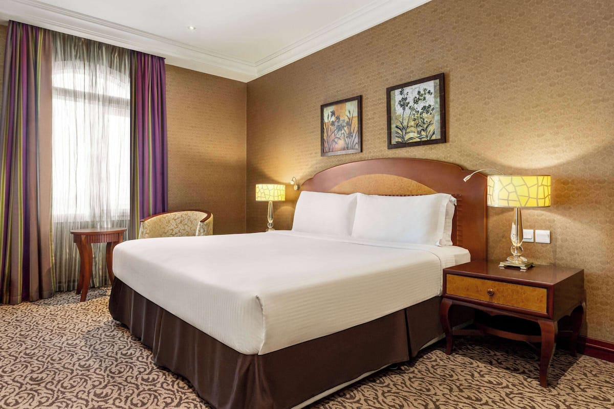 Habitación de hotel con una cama grande, dos mesitas de noche con lámparas, una pequeña mesa y dos cuadros en la pared.