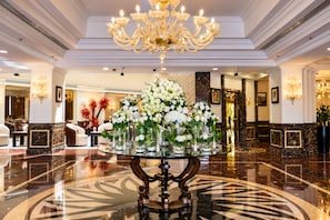 A lobby with a central table displaying floral arrangements, a chandelier, and marble flooring. - Grand Regency Doha, Trademark Collection by Wyndham (Doha)
