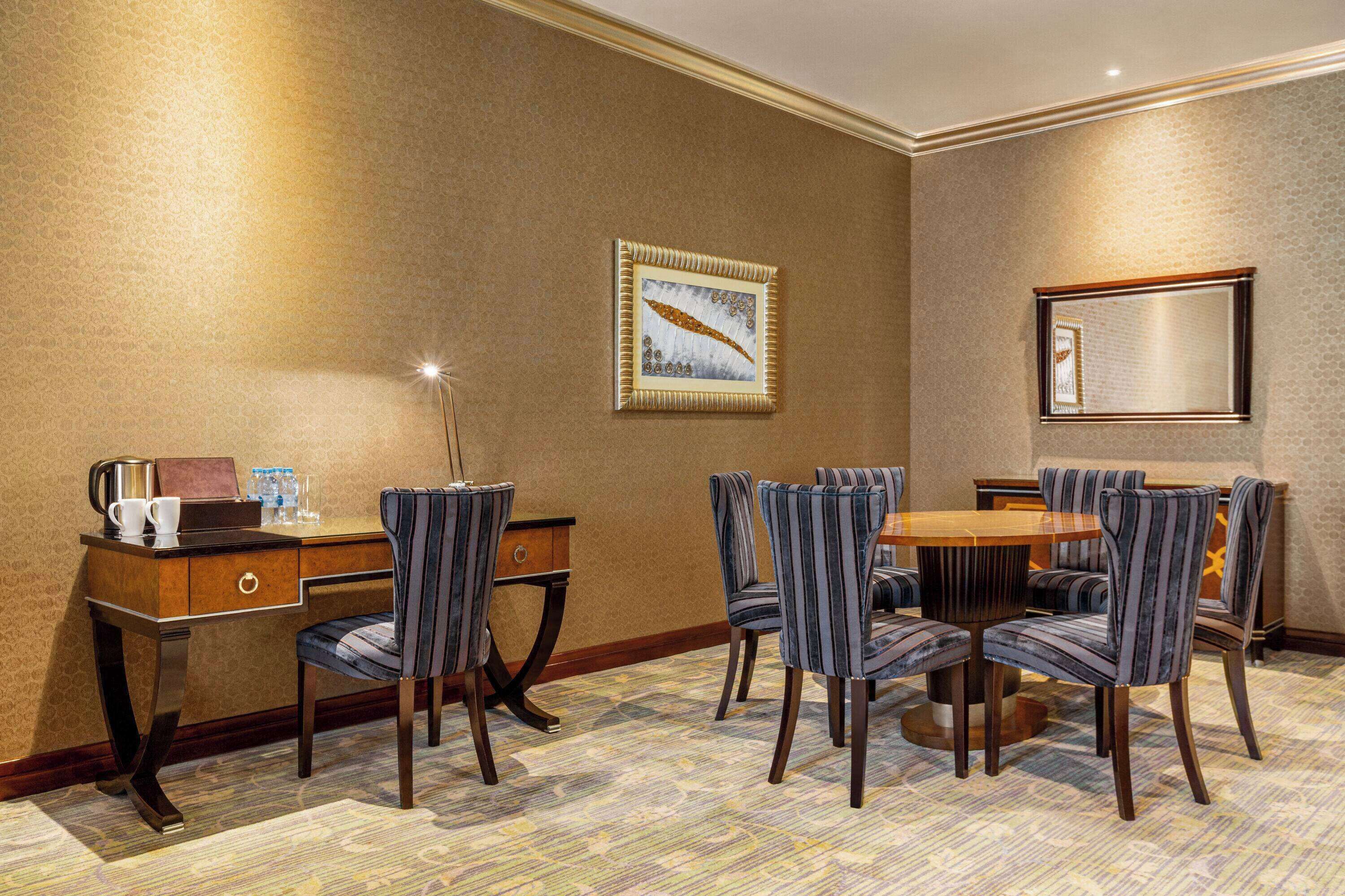 A hotel room with a dining area featuring a wooden table and six upholstered chairs.