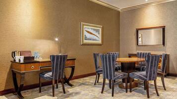 A hotel room with a dining area featuring a wooden table and six upholstered chairs.