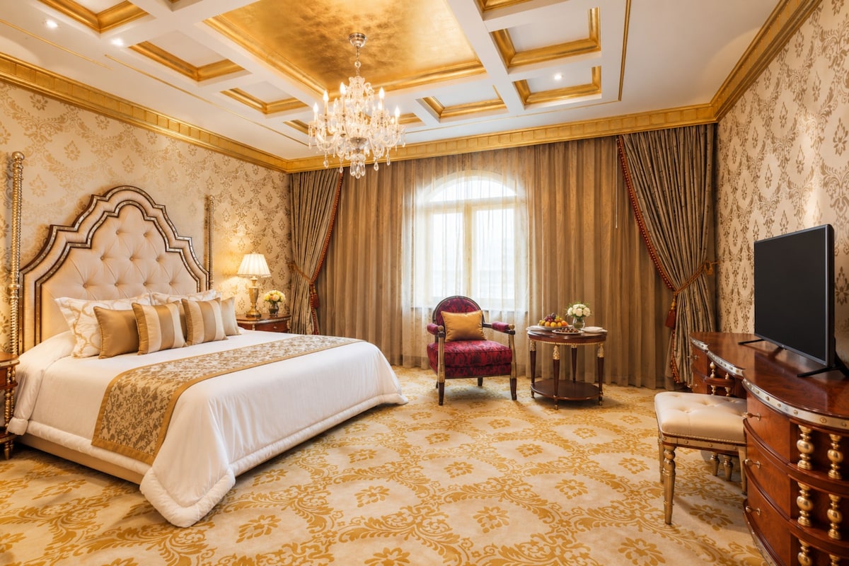 A luxurious hotel room with a large bed, a television, a desk, and a chair.