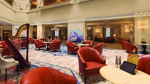 A spacious lobby with red leather seating, a harp, and a chandelier.
