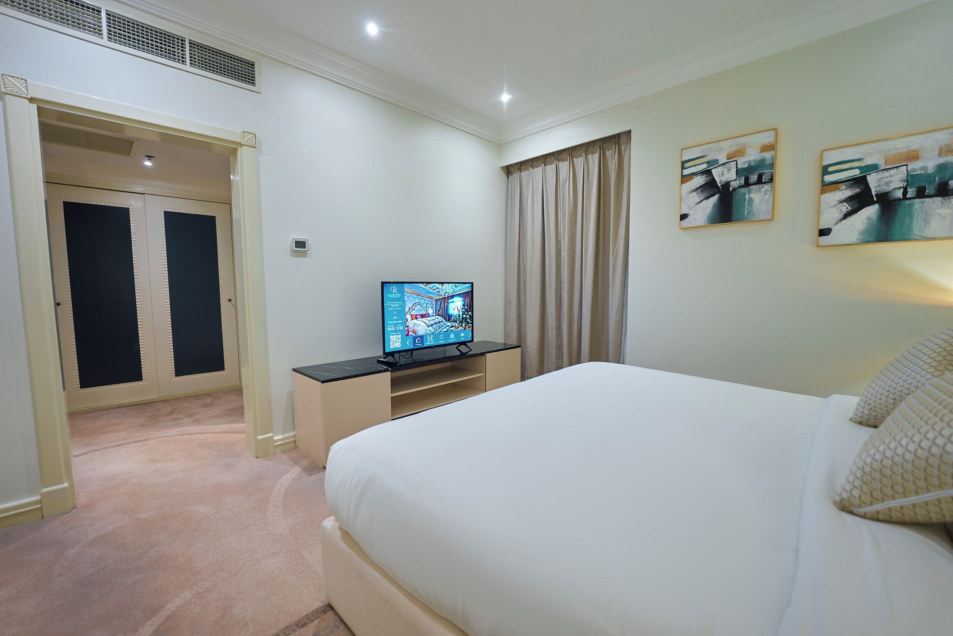 Habitación de hotel con cama, televisión, armario y dos cuadros en la pared.