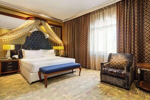 A hotel room with a large bed, a canopy bed, a chair, a nightstand, and a lamp. - Grand Regency Doha, Trademark Collection by Wyndham (Doha)