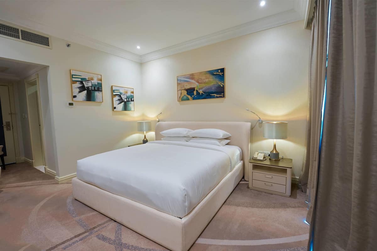Una habitación de hotel con una cama grande, dos mesitas de noche con lámparas y obras de arte en las paredes.
